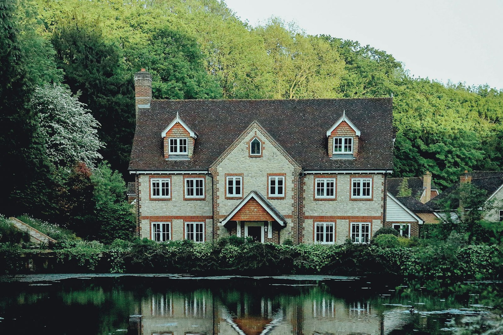 A heritage house with dormer windows surrounded by tall trees and still water (placeholder photo)